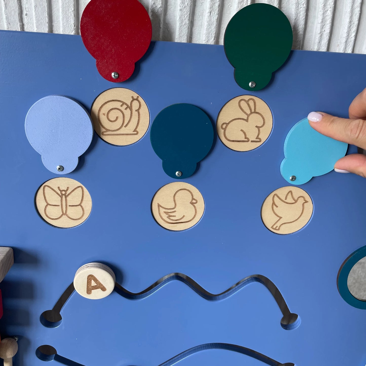 Interactive sensory board section with flip-up colored wooden circles revealing engraved animal silhouettes such as snail, bunny, butterfly, duck, and bird