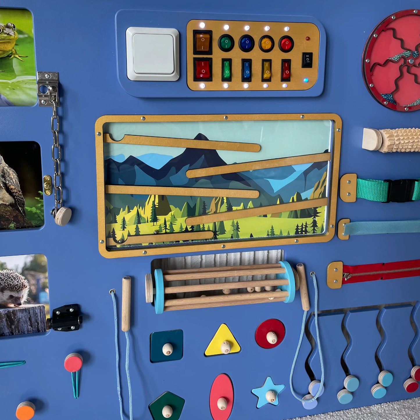 Close-up view of sensory panel featuring mountain-themed marble maze, colorful LED light switchboard, tactile roller, zippers, and fine motor skill elements