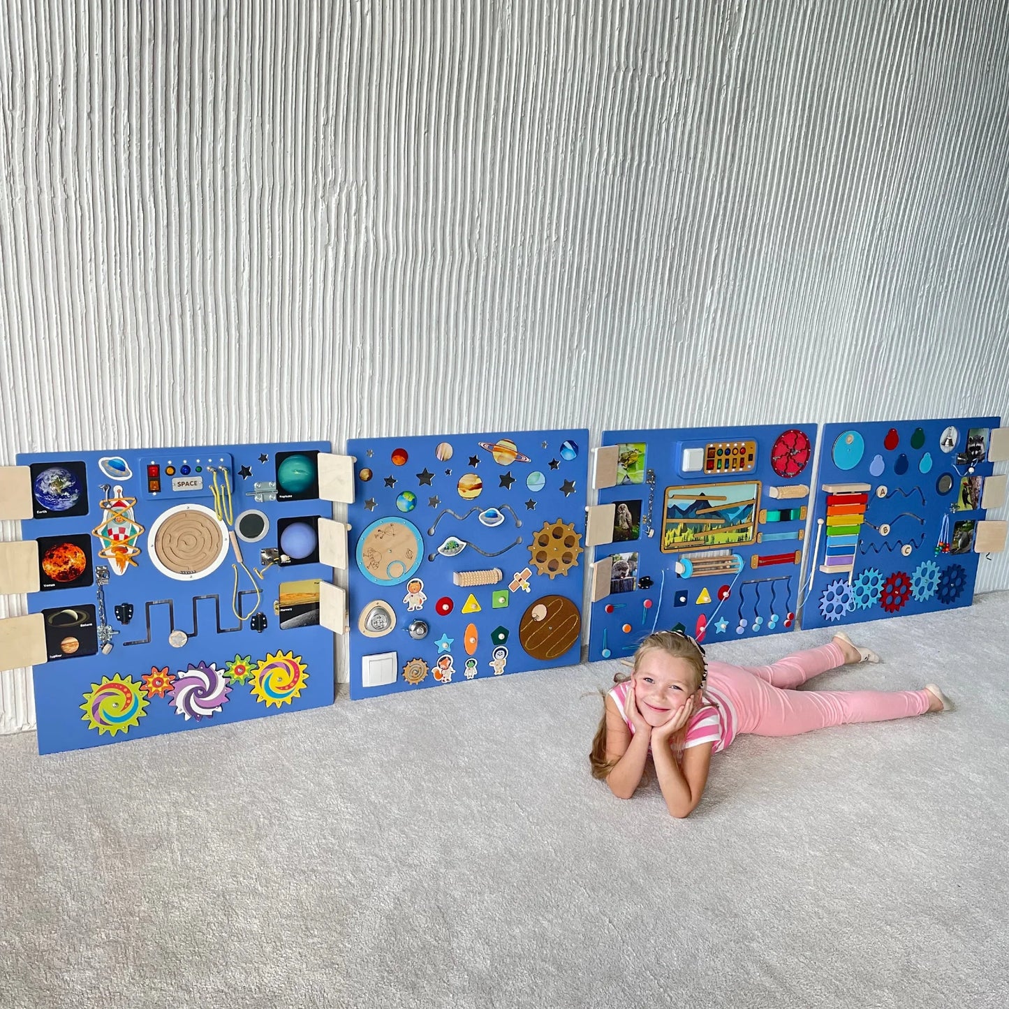Smiling girl lying on the floor in front of an extra-large deep purple sensory wall panel with lights and fine motor activities for kids with special needs or autism