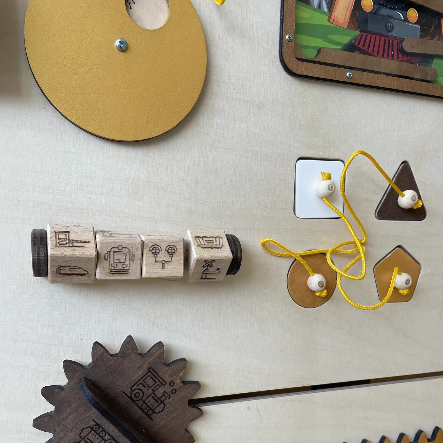 Detailed view of train-themed busy board showing rotating wooden cubes with train icons and a yellow lacing activity with different shapes