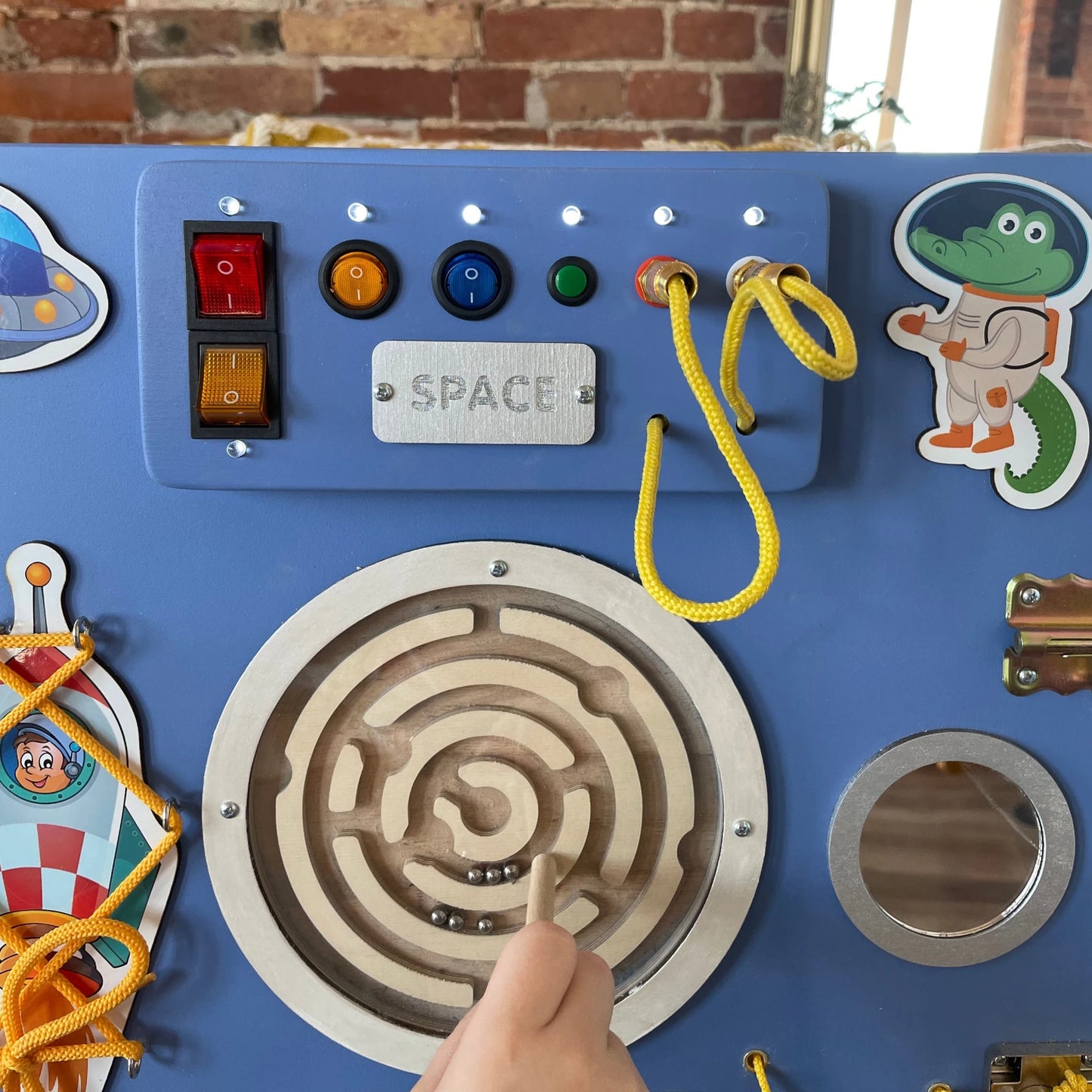 Close-up of a space-themed sensory wall panel showing maze, switches, LED lights, and cords. Great for fine motor skills and autism therapy
