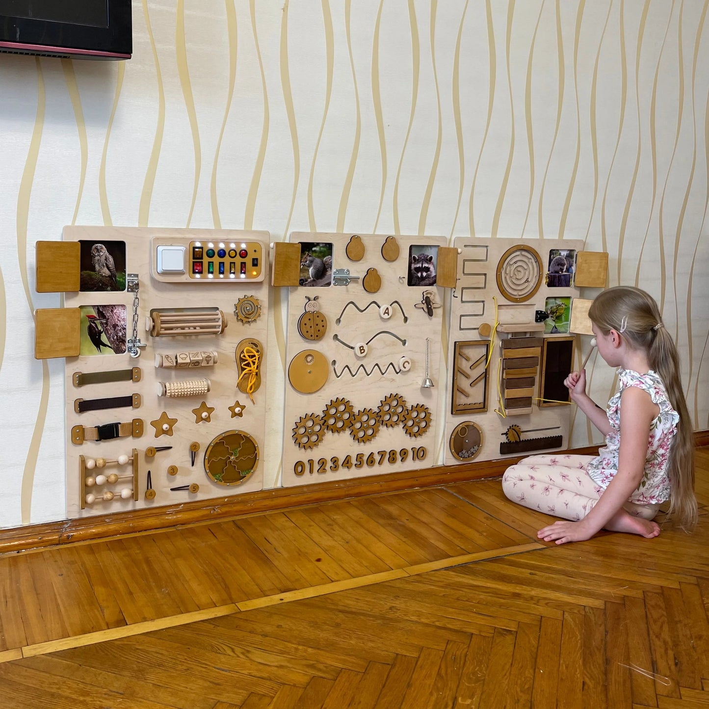 A girl playing with a large natural-color sensory wall panel mounted on the wall; perfect for fine motor development.