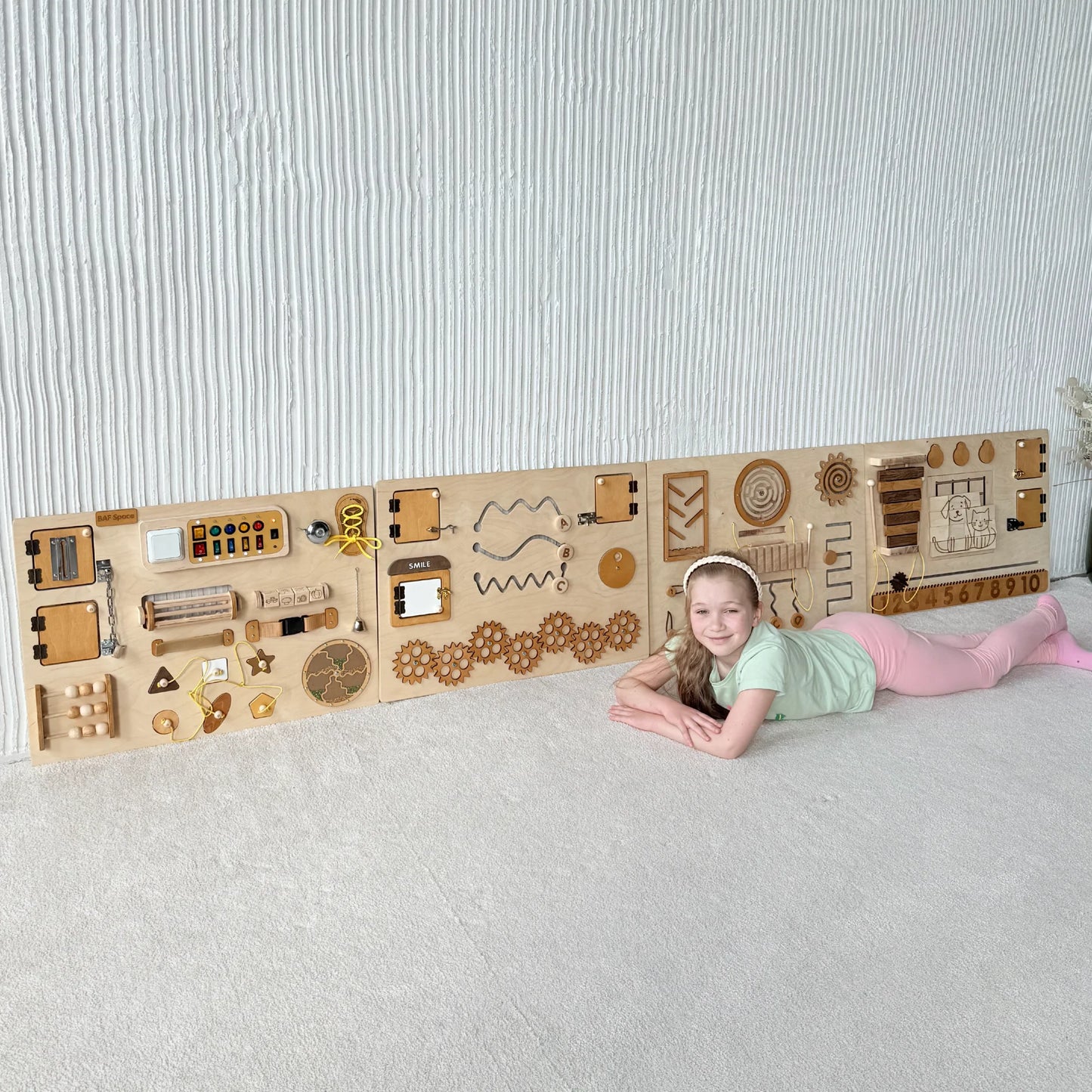 Girl lying in front of natural wood sensory wall panel with educational and fine motor elements
