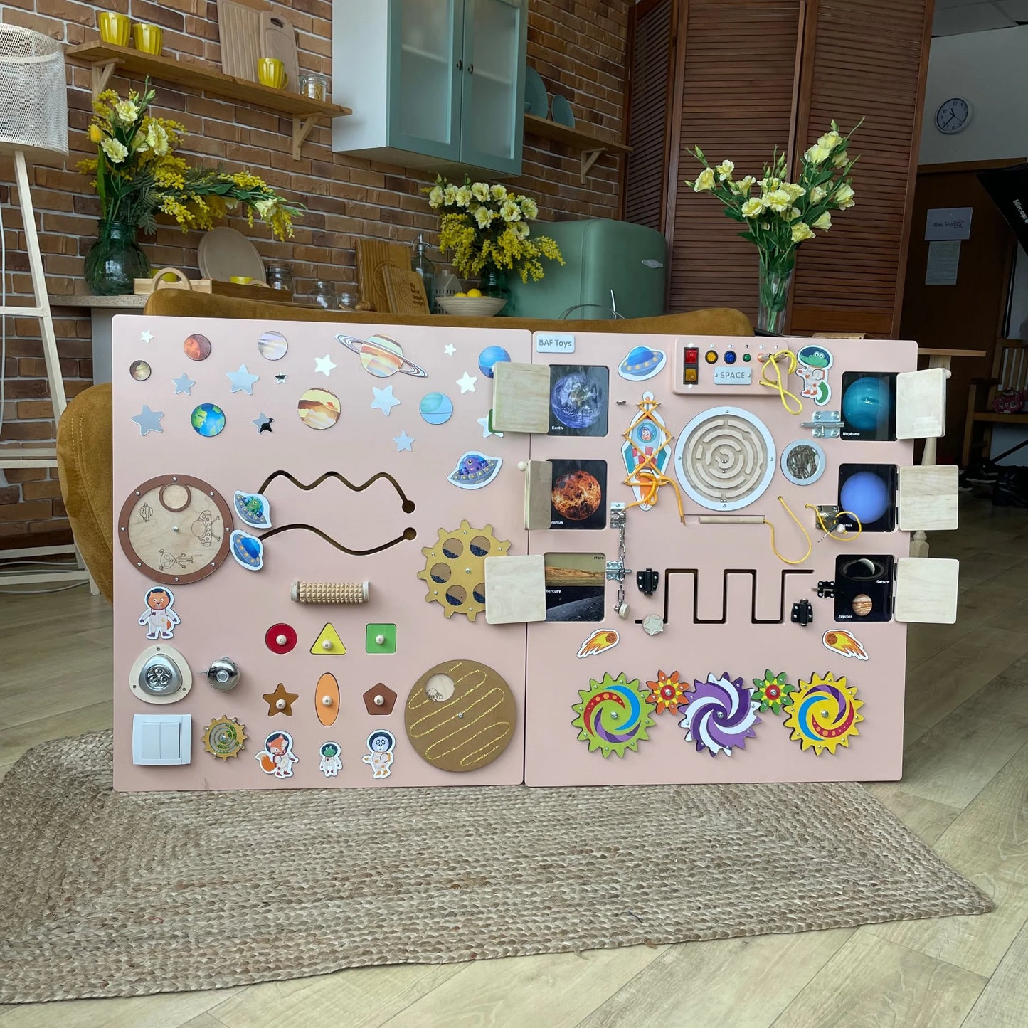 Pink sensory wall panel with space theme for preschool and therapy use. Includes doors, gears, LED lights, and tactile fine motor activities