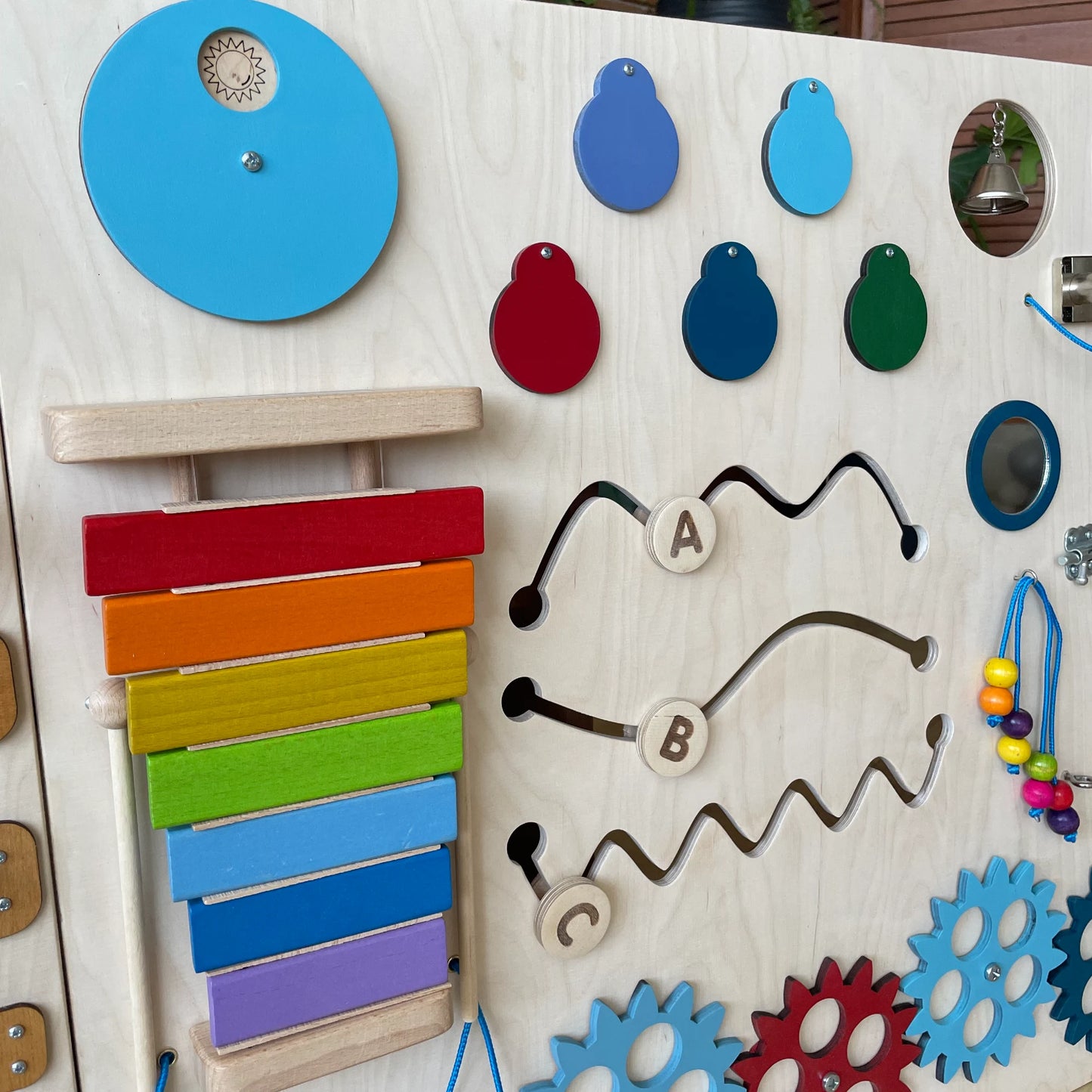 Rainbow xylophone and zigzag path elements on sensory board for color learning and fine motor skill development.