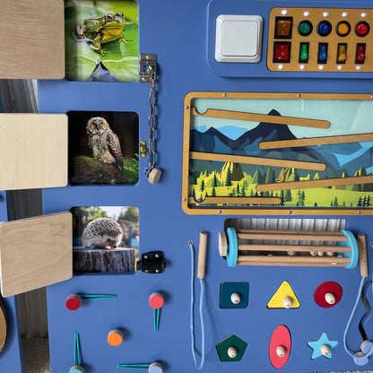 Close-up of wooden sensory wall showing animal cards behind doors, mountain-themed marble maze, toggle switches, and fine motor skill activities
