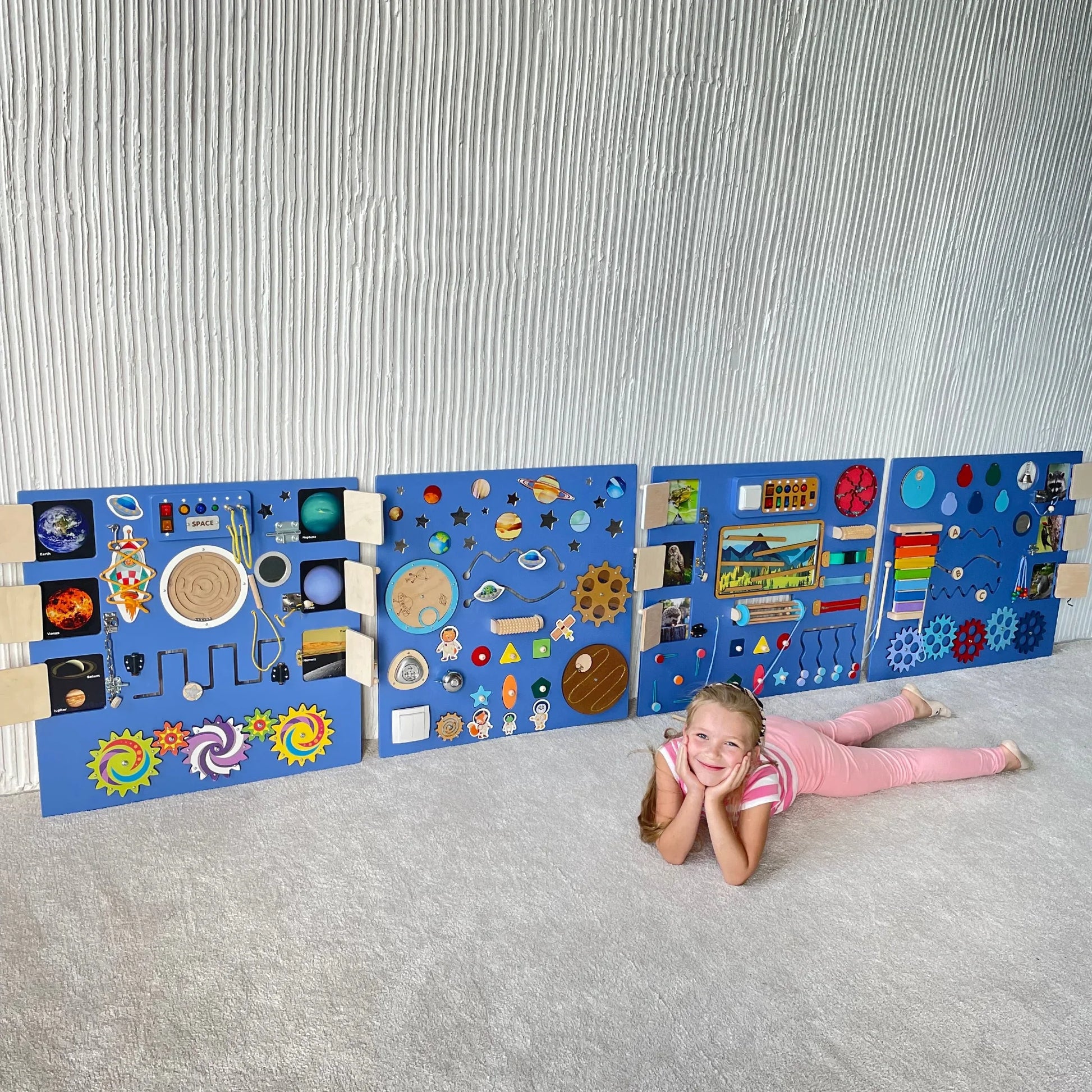 Smiling girl lying on the floor in front of an extra-large deep purple sensory wall panel with lights and fine motor activities for kids with special needs or autism
