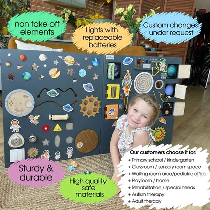 Smiling girl next to a large space-themed sensory wall panel with labeled features such as non-take-off elements, replaceable batteries, custom changes, and recommended uses for schools, clinics, and therapy

