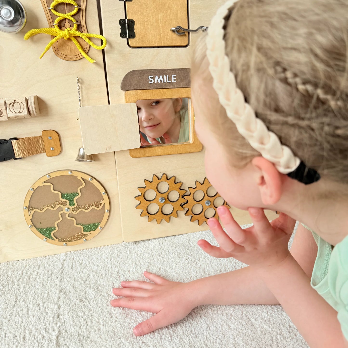 Close-up of sensory wall panel mirror with girl’s face reflected, gears and fine motor activities visible