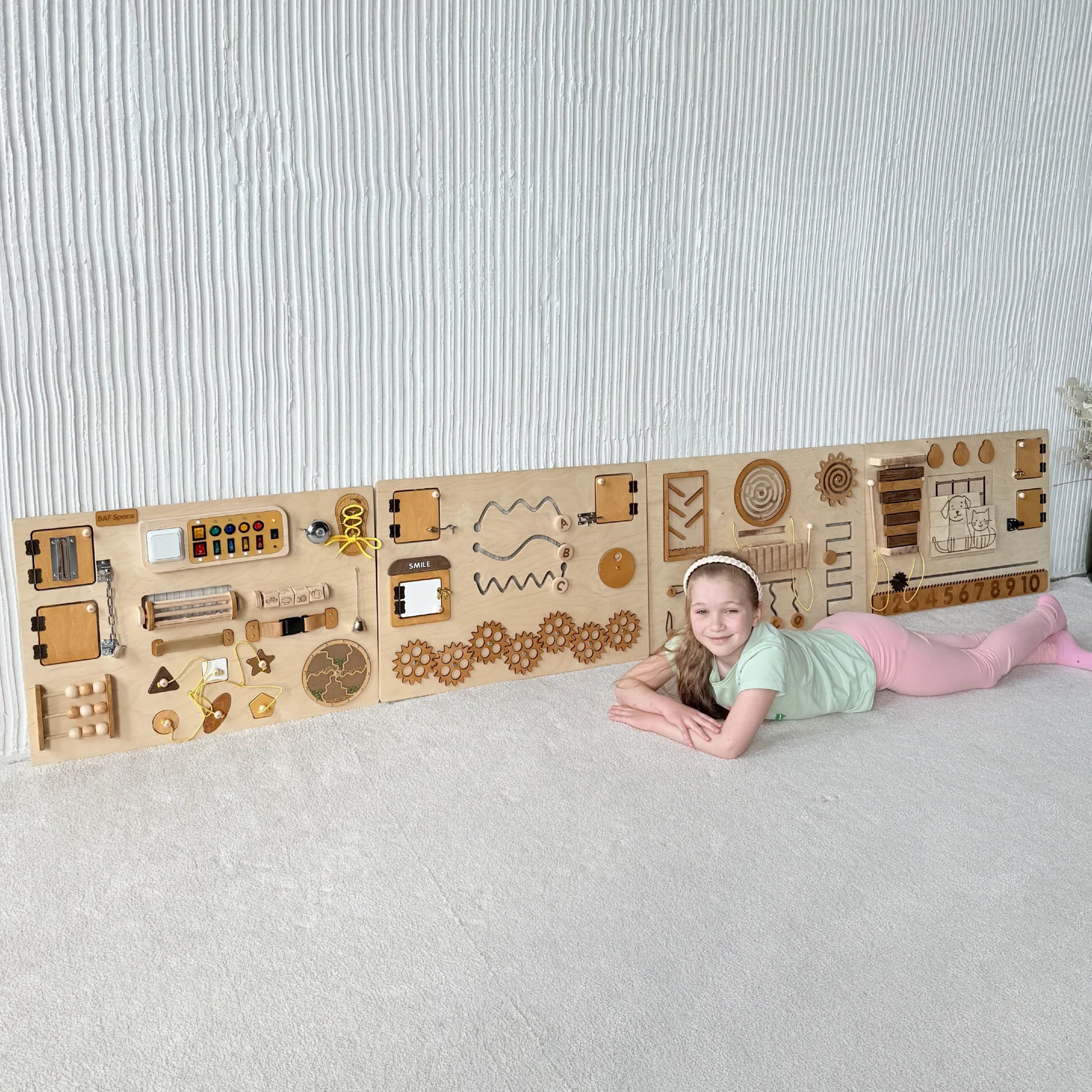 Girl lying in front of natural wood sensory wall panel with educational and fine motor elements