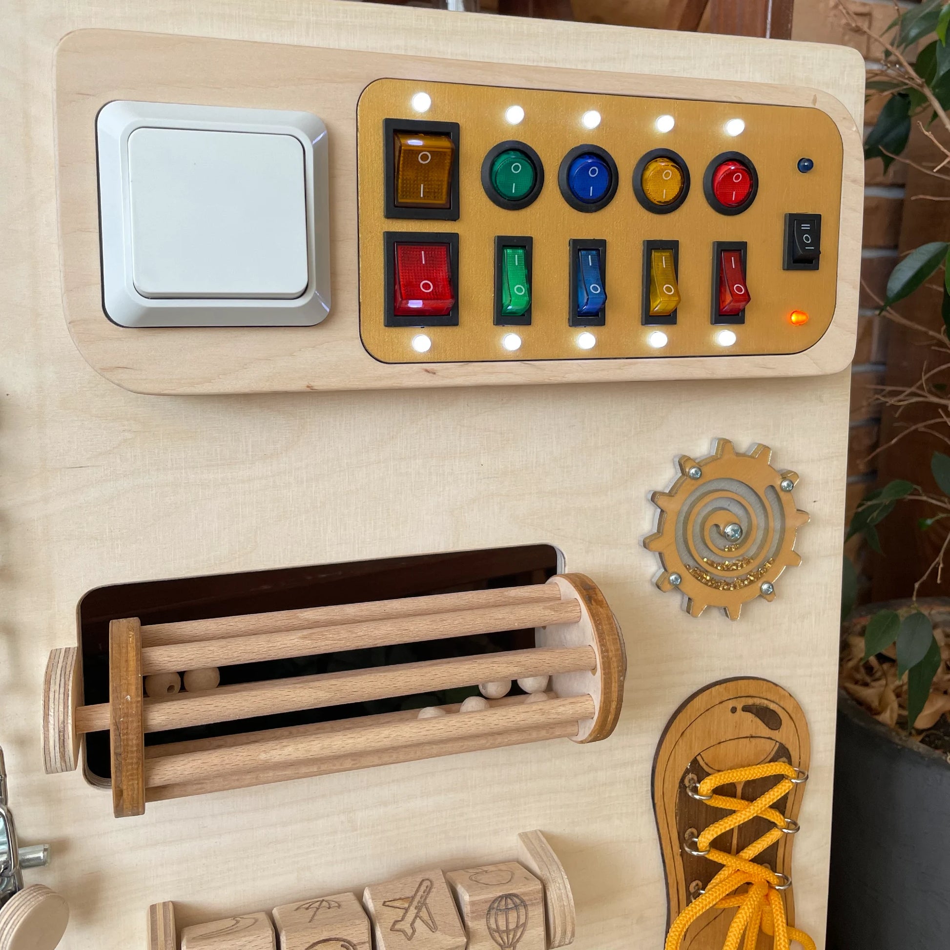 Close-up of the LED light switches section on the wooden sensory wall panel for tactile stimulation and cause-effect learning.